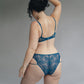 Back view of a model wearing a teal blue lace bralette and bikini with double mini straps details
