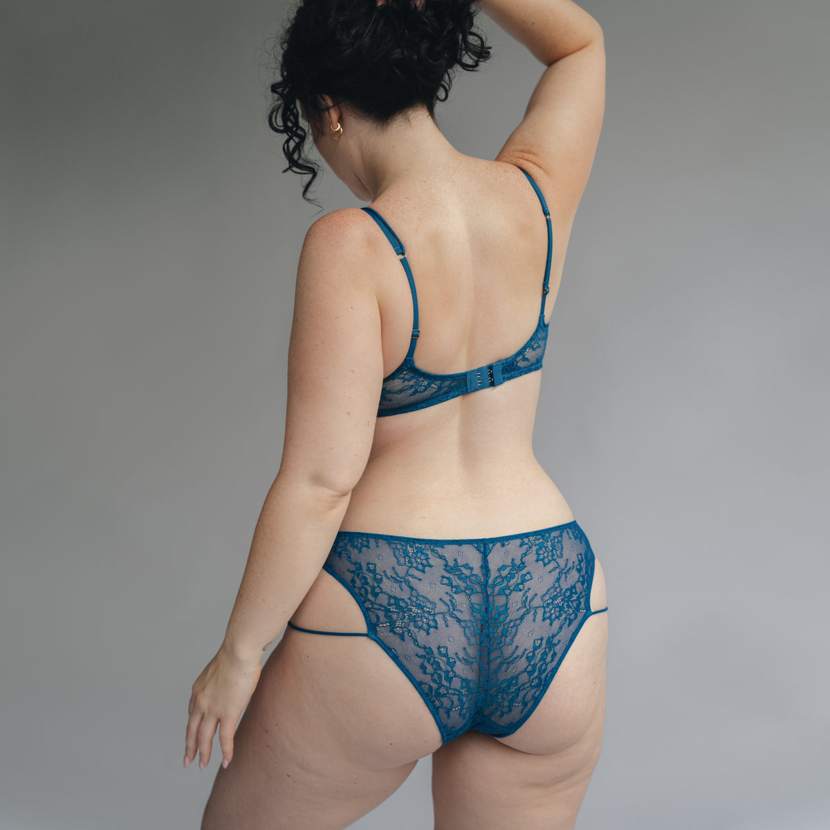 Back view of a model wearing a teal blue lace bralette and bikini with double mini straps details