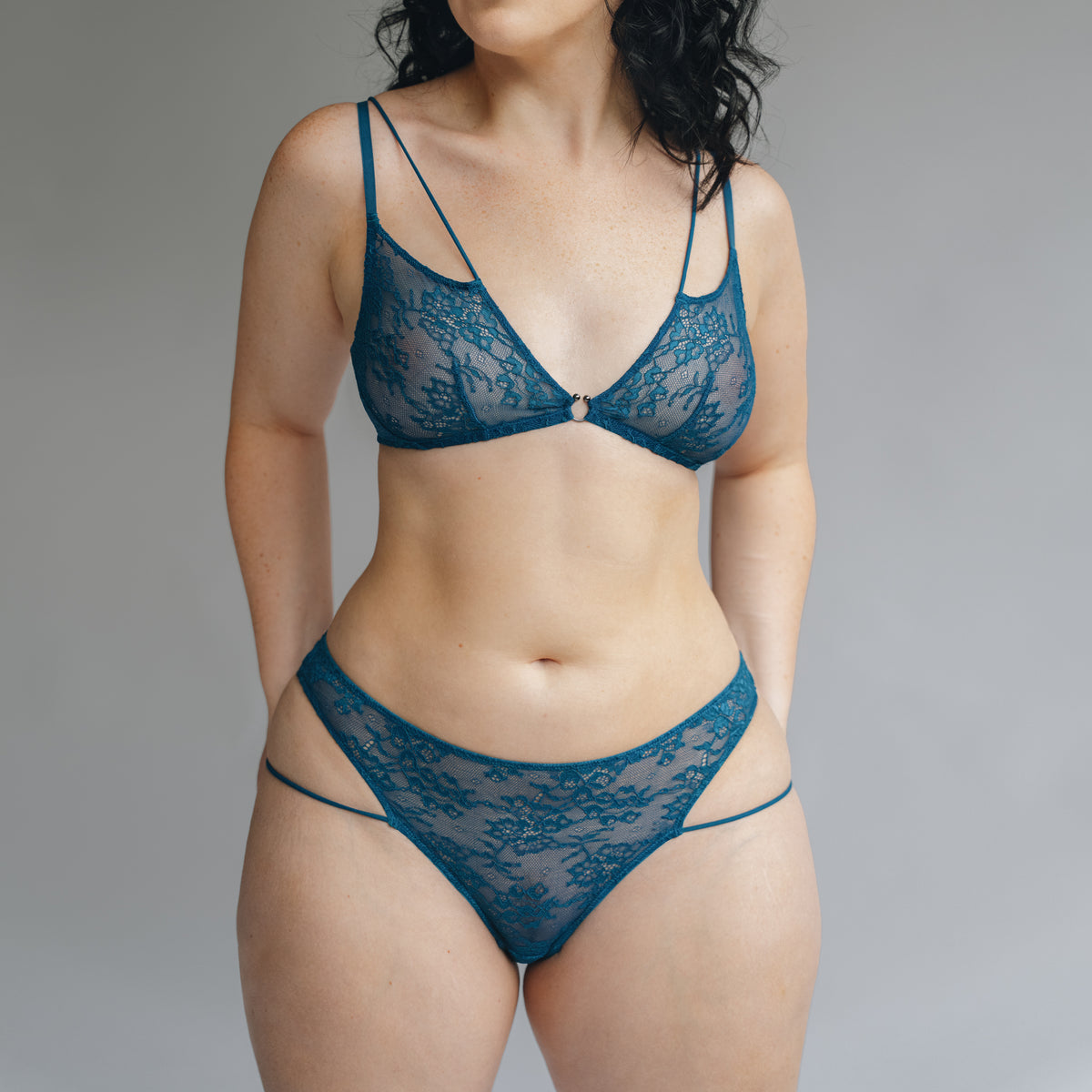 Front view of a model wearing a teal blue lace bralette and bikini with double mini straps details