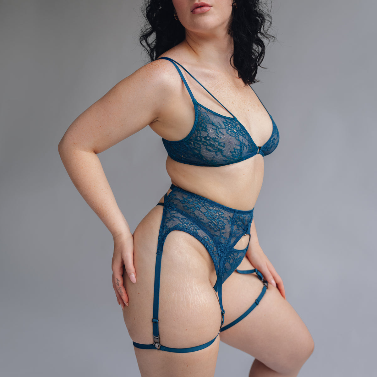 side view of model wearing a teal blue lace bralette garter belt and thong