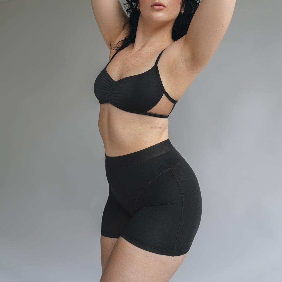 Side view of a model wearing a black bralette with center front ruching and a high waisted women boxer in black with front seaming detail and wide elastic band