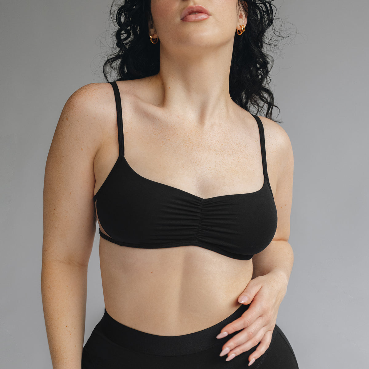 Model wearing a black bralette with center front ruching and sheer mesh insert at sides