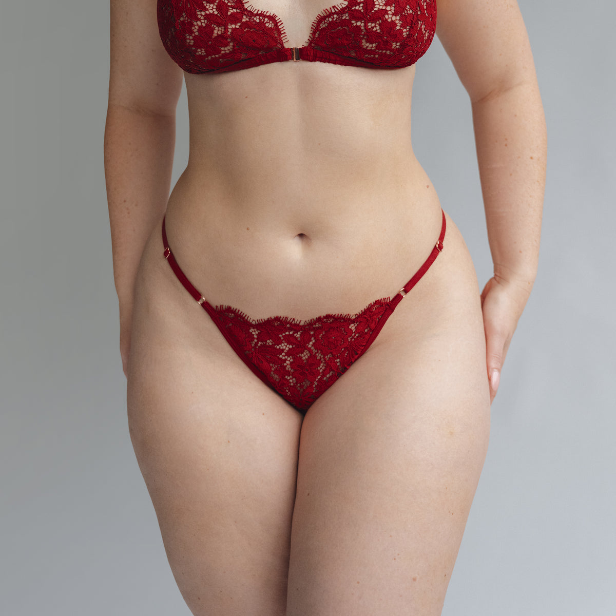 Model wearing a red lace thong with adjustable waist elastics