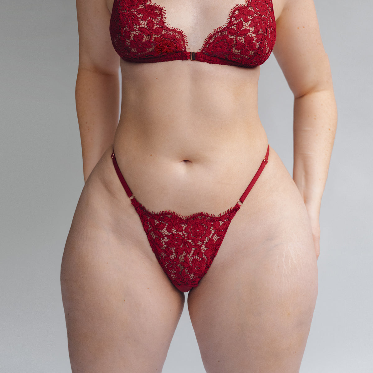 Model wearing deep red lace thong with adjustable waist straps;